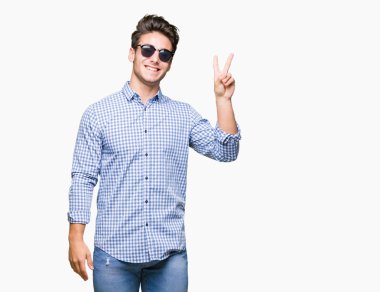 Genç yakışıklı adam mutlu yüz zafer işareti yaparken kameraya göz kırpıyor ile gülümseyen izole arka plan üzerinde güneş gözlüğü takıyor. İki numaralı.