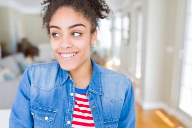 Afro saçlı rahat denim ceket görünümlü yan ve dik dik bakma uzağa düşünce gülümseyen güzel genç Afro-Amerikan kadın.