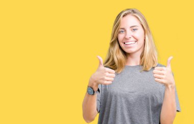 El ile pozitif jest yapıyor izole arka plan başarı işareti üzerinde büyük boy rahat t-shirt giyen güzel ve genç birbayan başparmak gülümseyen ve mutlu. Neşeli bir ifadeyle, kazanan jest kameraya bakıyor.