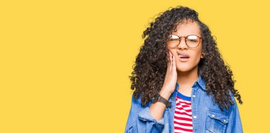 Genç güzel kadın kıvırcık saçlı gözlüklü diş ağrısı veya dişlerde dişlerle ilgili hastalık nedeniyle ağız acı ifadesi ile el ile dokunmak. Diş hekimi kavramı.