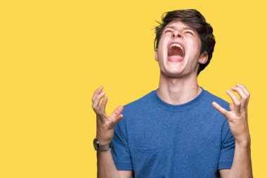 Üzerinde mavi t-shirt giyen genç yakışıklı adam arka plan deli izole ve deli bağırarak ve agresif ifade ve silah kaldırdı bağırıyor. Hayal kırıklığı kavramı.