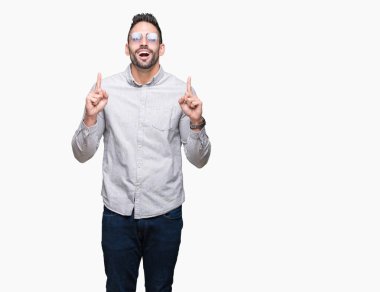 Yakışıklı delikanlı hayrete ve yukarıya bakıyor ve parmakları ile işaret ve silah kaldırdı sürpriz izole arka plan üzerinde güneş gözlüğü takıyor.