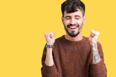 Zafer kutluyor gülümseyen izole arka kolları olan başarı için heyecan üzerinde kış kazak giyen genç yakışıklı adam kaldırdı. Kazanan kavramı.