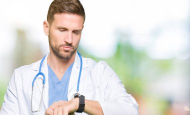 Handsome doctor man wearing medical uniform over isolated background Checking the time on wrist watch, relaxed and confident clipart
