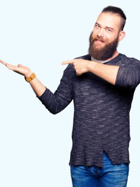 Genç Sarışın giyen sıradan kazak hayret ve el ile sunulması ve parmak ile işaret ederken kameraya gülümseyen adam.