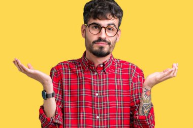 İzole arka plan clueless ve şaşkın bir ifadeyle kollar ve eller kaldırdı üzerinde gözlük takan yakışıklı delikanlı. Şüphe kavramı.