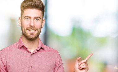 Kameraya bakarak yan el ve parmak ile işaret eden genç yakışıklı iş casual adam yüzünde kocaman bir gülümseme ile.