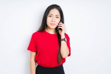 Genç esmer kadın akıllı yüz ciddi düşünme kendinden emin bir ifade ile izole arka plan üzerinde akıllı telefon konuşuyor