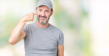 Handsome middle age hoary senior man wearing sport cap over isolated background Pointing with hand finger to face and nose, smiling cheerful clipart