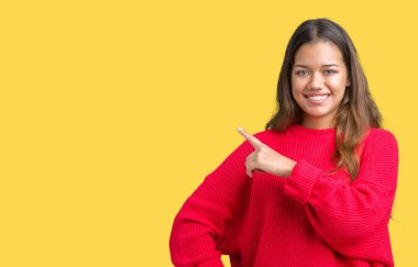 Üzerinde izole kırmızı kış kazak giyen genç güzel esmer kadın yan gösteren reklam, ciddi ve sakin yüz el parmak ile işaret arka plan