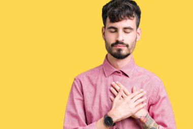 Yakışıklı delikanlı ile gülümseyen izole arka plan üzerinde pembe gömlek giymiş kapalı gözler ve yüzünde minnettar jest ile göğüs üzerinde eller. Sağlık kavramı.