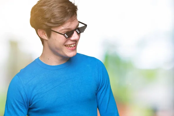 Young man wearing funny thug life glasses over isolated background looking away to side with smile on face, natural expression. Laughing confident.