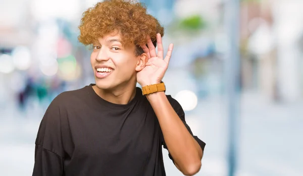 年轻的帅哥 穿着黑色T恤微笑 手在耳朵上听听谣言或八卦 耳聋概念 — 图库照片