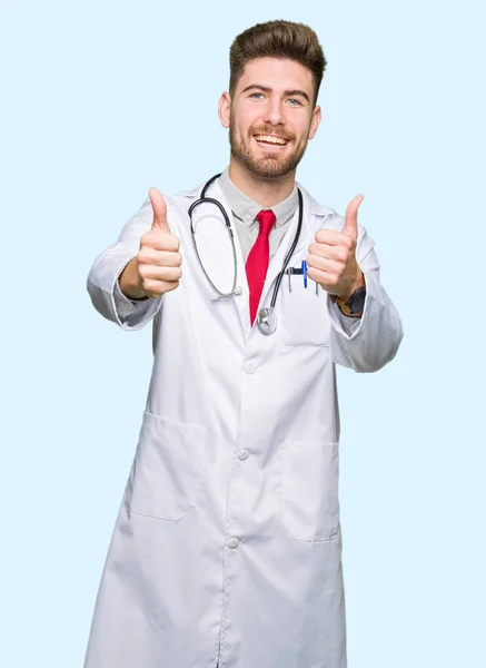 年轻英俊的医生穿着医疗外套 赞成用手做积极的手势 竖起大拇指微笑 为成功而高兴 看着镜头 赢家的手势 — 图库照片