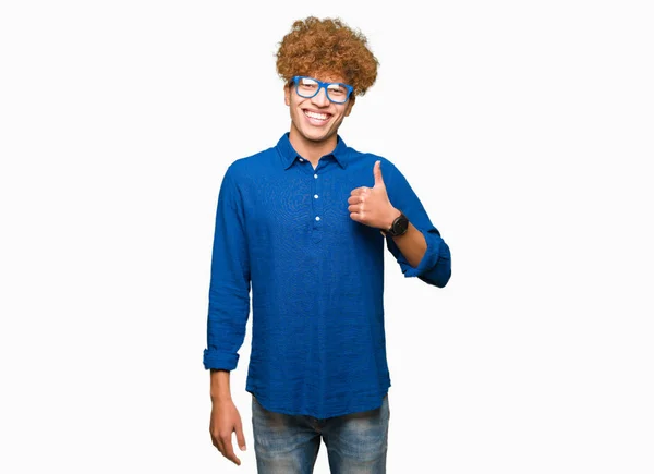 年轻英俊的男子与非洲头发蓝色眼镜做快乐的大拇指与手的手势 通过显示成功来批准镜头的表达 — 图库照片