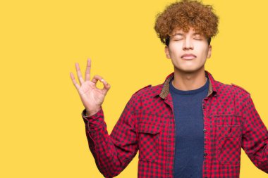 Afro saçlı bir ceket giyen genç yakışıklı öğrenci adam rahatla ve gülümseyen gözlerle kapalı parmak jestle meditasyon yapıyor. Yoga kavramı.