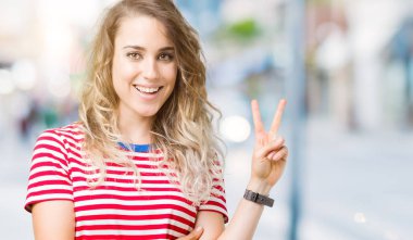 Güzel sarışın genç kadın mutlu yüz zafer işareti yaparken kameraya göz kırpıyor ile gülümseyen izole arka plan üzerinde. İki numaralı.