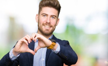 Kalp simgesi ve elleriyle şekil gösterilen aşık gülümseyen genç yakışıklı iş adam. Romantik kavramı.