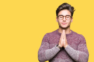 Ellerle birlikte AF emin gülümseyen için soran dua izole arka plan üzerinde gözlük takan genç yakışıklı adam.