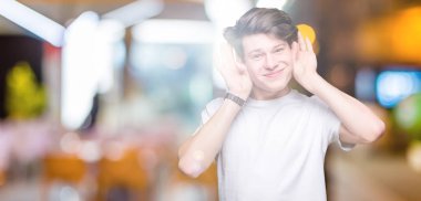 Her ikisi de dinliyoruz izole arka plan üzerinde rahat beyaz t-shirt giyen genç yakışıklı adam kulak jest, dedikodu için meraklı eller. İşitme sorunu, sağır