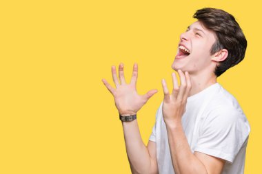 Üzerinde rahat beyaz t-shirt giyen genç yakışıklı adam arka plan deli izole ve deli bağırarak ve agresif ifade ve silah kaldırdı bağırıyor. Hayal kırıklığı kavramı.