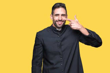 Genç Hıristiyan rahip izole üzerinde arka plan işaretçi el parmak yüz ve burun, neşeli gülümseyen