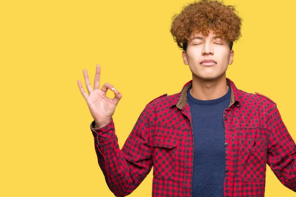 Afro saçlı bir ceket giyen genç yakışıklı öğrenci adam rahatla ve gülümseyen gözlerle kapalı parmak jestle meditasyon yapıyor. Yoga kavramı.