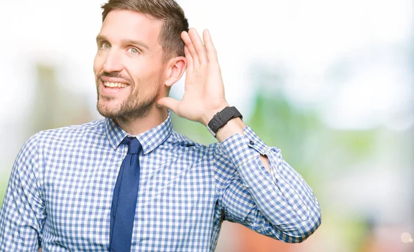 Handsome business man wearing tie smiling with hand over ear listening an hearing to rumor or gossip. Deafness concept.