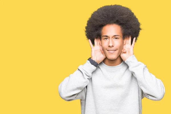 年轻的非洲裔美国人与非洲头发穿着运动的运动运动衫试图听到双手对耳朵手势 好奇八卦 听力问题 — 图库照片