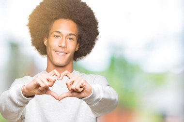 Afrikalı-Amerikalı genç afro saçlı aşık kalp simgesi ve elleriyle şekil gösteren gülümseyen sportif kazak giyiyor. Romantik kavramı.
