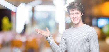 Neşeli sunulması ve kameraya bakarak avucunun ile işaret gülümseyen izole arka plan üzerinde kış kazak giyen genç yakışıklı adam.