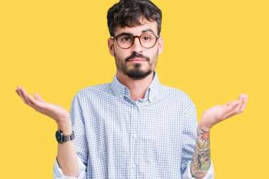 İzole arka plan clueless ve şaşkın bir ifadeyle kollar ve eller kaldırdı üzerinde gözlük takan yakışıklı delikanlı. Şüphe kavramı.