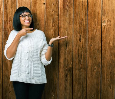 Güzel genç Afro-Amerikan kadın hayrete ve el ile sunulması ve parmak ile işaret ederken kameraya gülümseyen izole arka plan üzerinde gözlük.