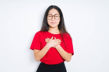 Güzel esmer kadın kapalı gözleri ve yüzünde minnettar jest ile göğüs üzerinde elleri ile gülümseyerek izole arka plan üzerinde gözlük takan. Sağlık kavramı.