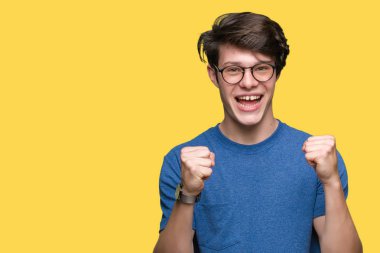 Yakışıklı delikanlı izole arka plan üzerinde kutluyor gözlük takan şaşırttı ve başarı için kaldırdı kollarını açarak hayret ve gözleri açık. Kazanan kavramı.