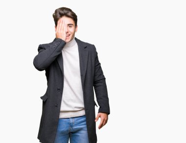 Yüz ve sürpriz duygu kendine güvenen gülümseme ile el ile bir göz kaplayan izole arka plan üzerinde kış ceket giyen genç zarif adam.