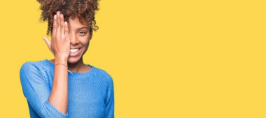 El yüz ve sürpriz duygu kendinden emin gülümseme ile tek gözüyle kapsayan izole arka plan güzel genç Afro-Amerikan kadın.