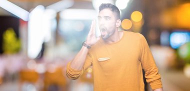 Yakışıklı delikanlı bağırarak ve ağzı üzerinde el ile yan için çığlık izole arka plan üzerinde. İletişim kavramı.