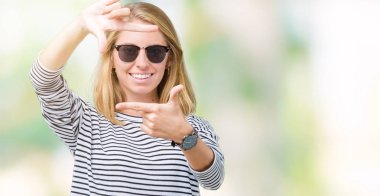 Güzel genç kadın elle yapma çerçeve ve parmakları ile mutlu yüz gülümseyen izole arka plan üzerinde güneş gözlüğü takıyor. Yaratıcılık ve Fotoğrafçılık kavramı.