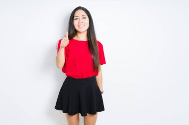 Güzel esmer kadın kırmızı t-shirt ve izole arka plan üzerinde etek giyen el ile jest kadar mutlu başparmak yapıyor. Başarı gösteren kameraya bakarak ifadeyi onaylama.