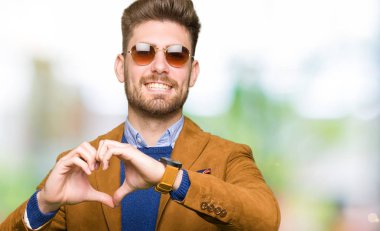 Genç yakışıklı zarif adam aşık kalp simgesi ve elleriyle şekil gösteren gülümseyen güneş gözlüğü takıyor. Romantik kavramı.