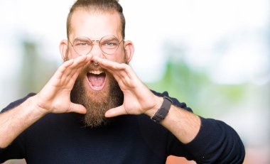 Gözlük ve kızgın ile yüksek sesle bağırarak boğazlı kazak giyen genç sarışın adam ağzına eller