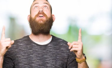 Casual kazak giyen genç sarışın adam hayret ve yukarıya bakıyor ve parmakları ile işaret ve silah kaldırdı şaşırttı.