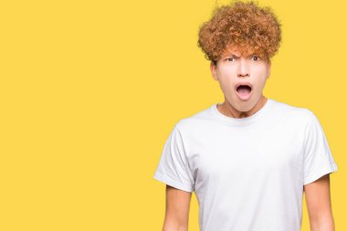 Casual beyaz giyen afro saçlı Genç yakışıklı adam şok karşısında şüpheci ve alaycı, t-shirt açık ağız ile şaşırttı.