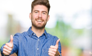 Genç yakışıklı sarışın adam el ile olumlu jest yapıyor onaylayan rahat kot gömlek giyen, gülümseyerek kadar başparmak ve başarı için mutlu. Kameraya bakmak, kazanan jest.
