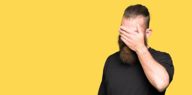 Genç sarışın adam rahat t-shirt gülümseyen giyen ve sürpriz için gözleri kapsayan yüzünde el ile gülüyor. Kör kavram.