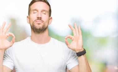 Casual beyaz t-shirt dinlenmek giydiği ve gözleri ile gülümseyen yakışıklı adam parmak ile meditasyon jest yapıyor kapalı. Yoga kavramı.