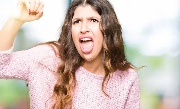 若くてきれいな女性身に着けているピンクのセーター怒っている 怒ってイライラして怒りで叫びながら激怒の拳を上げます 怒りと攻撃的な概念 — ストック写真