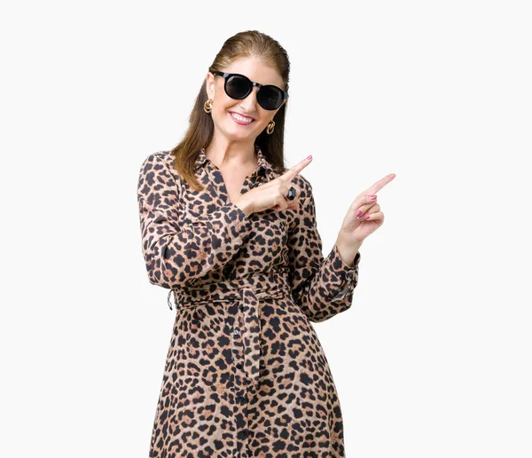 中年成熟した豊かな女性にサングラスとヒョウの服を着て笑顔で側に つの手と指で指しているカメラ目線の背景を分離しました — ストック写真