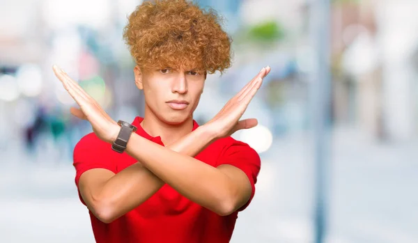 赤いTシャツを着たアフロヘアの若いハンサムな男は 否定的なサインをして腕を横切る表情を拒絶し 怒った顔 — ストック写真